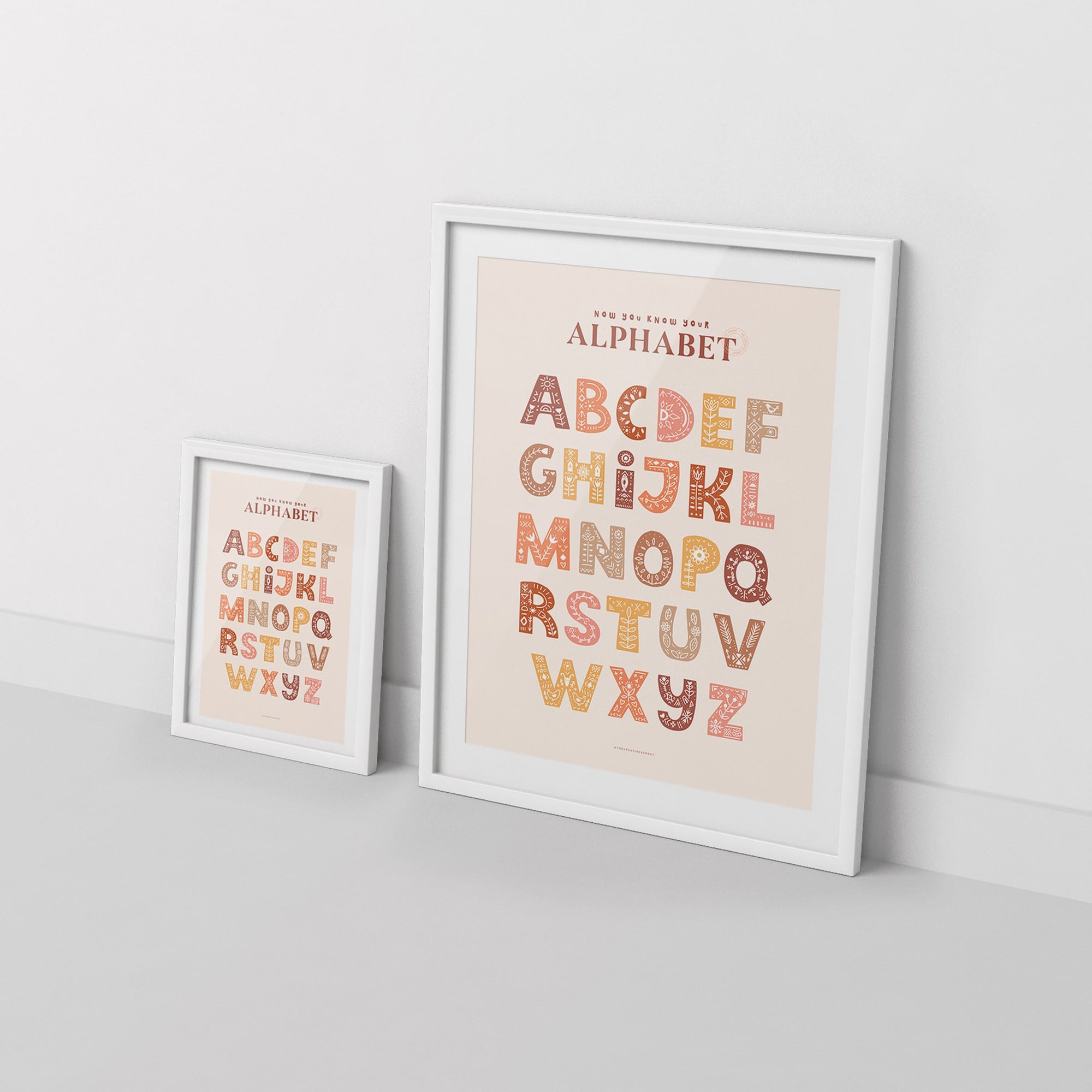 2 framed alphabet posters in boho style, leaning against white wall