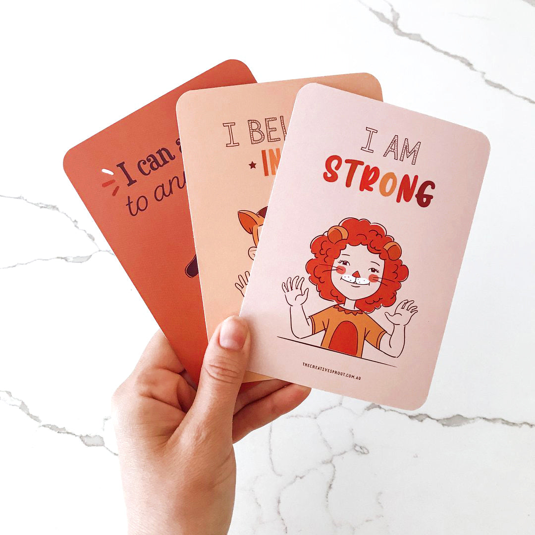 child's hand holding 3 positive affirmation cards
