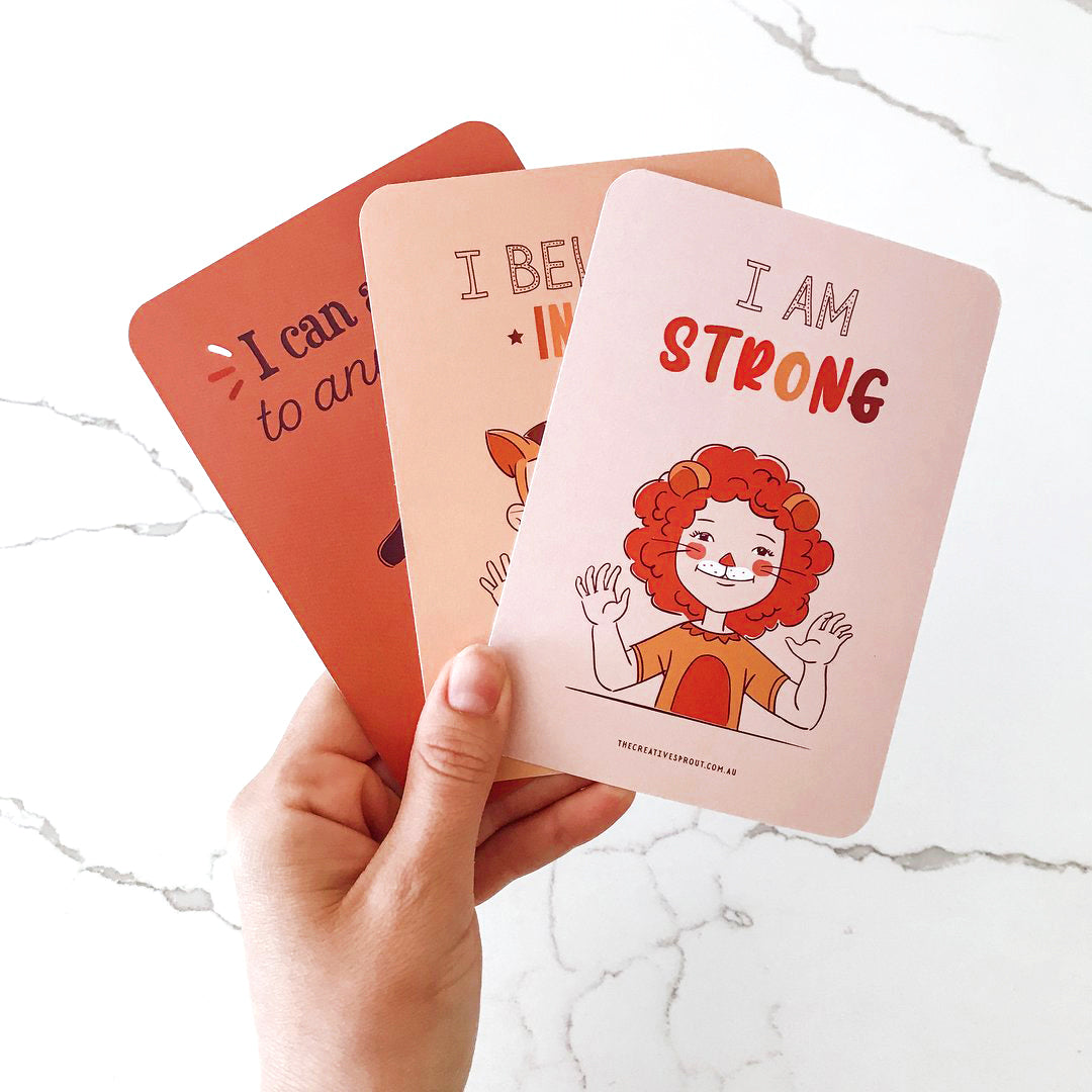 child&#39;s hand holding 3 positive affirmation cards