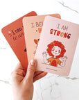 child's hand holding 3 positive affirmation cards